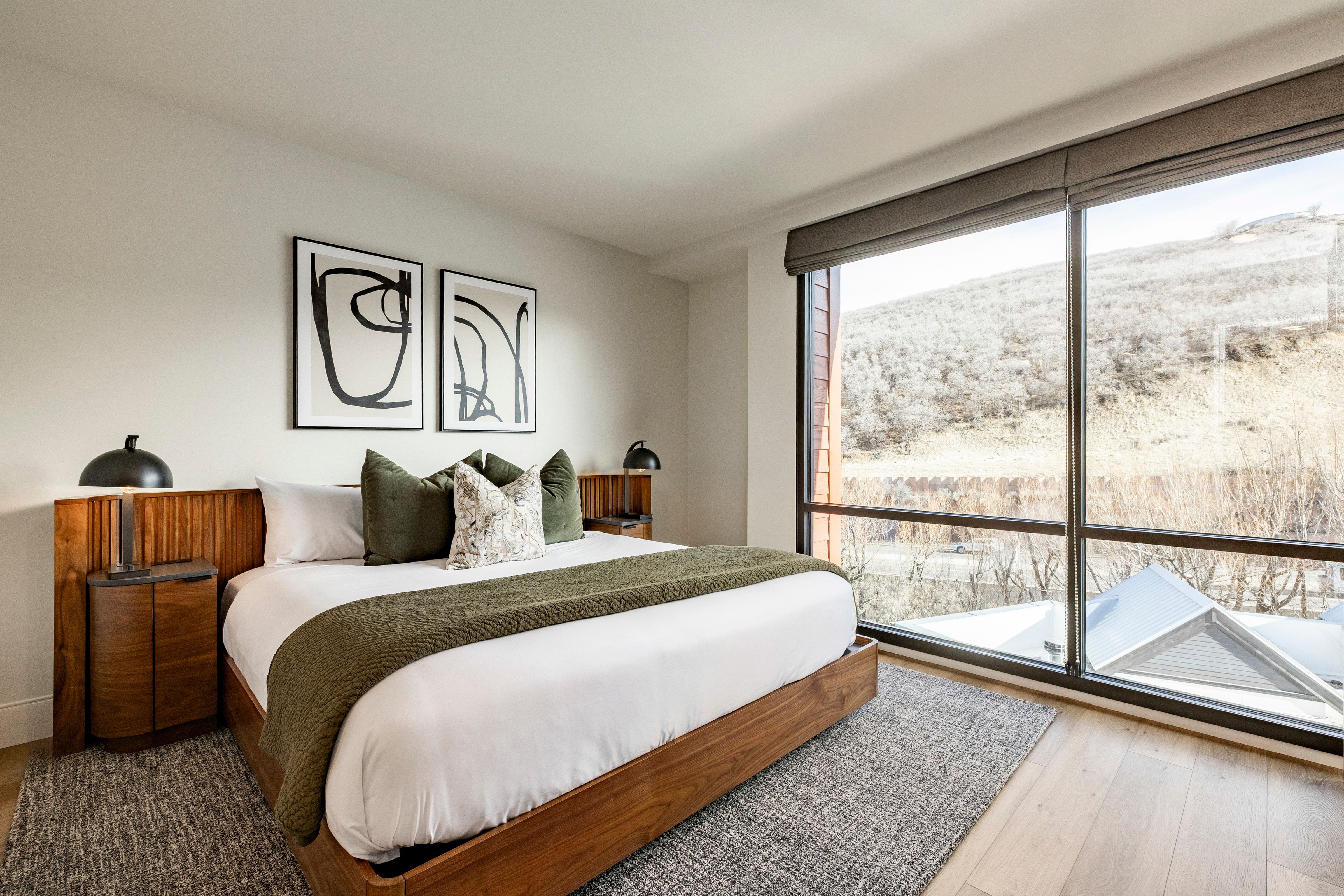 A hotel room with a large bed, a window, and artwork on the wall.