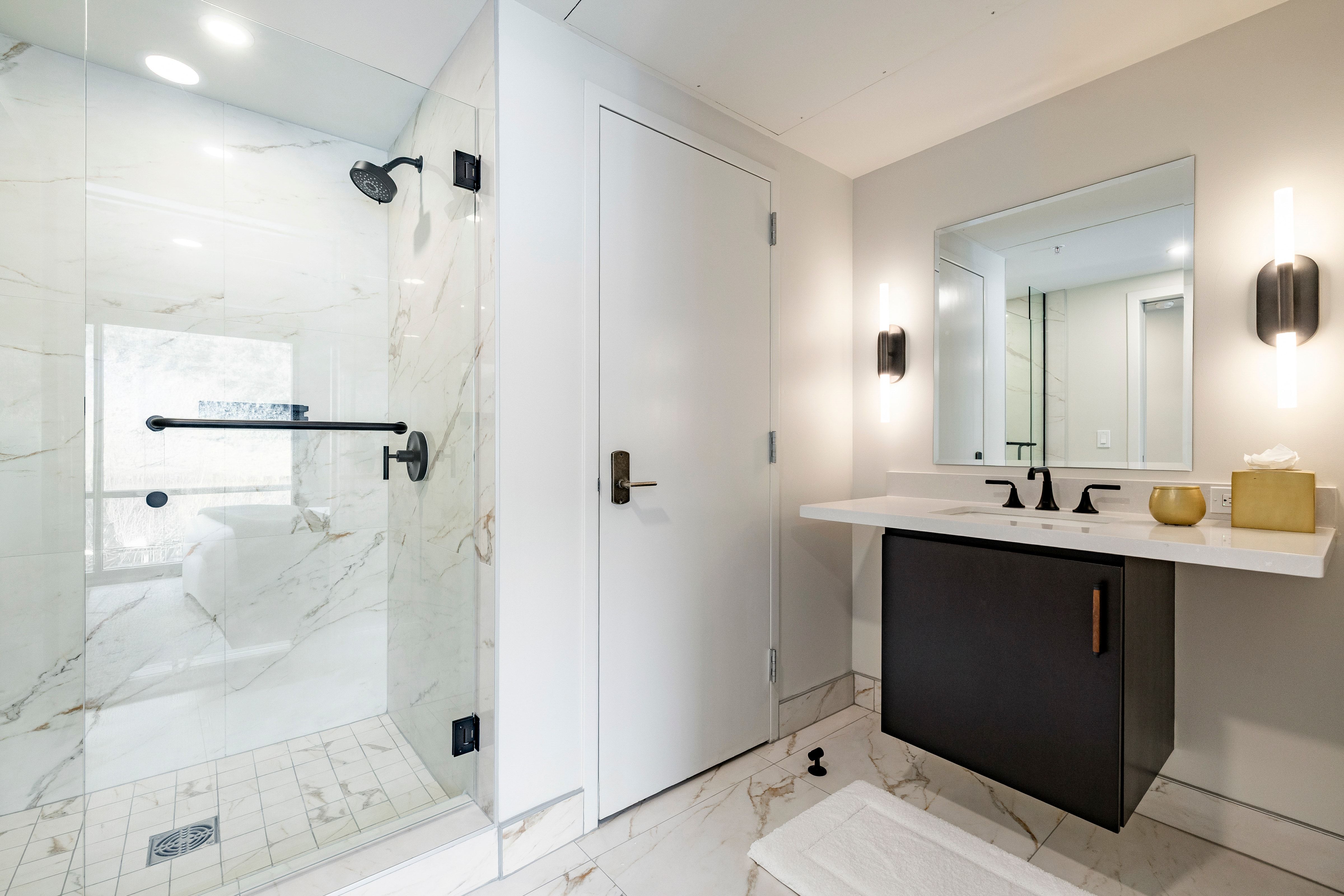 A modern bathroom with a glass shower, marble tiles, and a white sink with a large mirror.