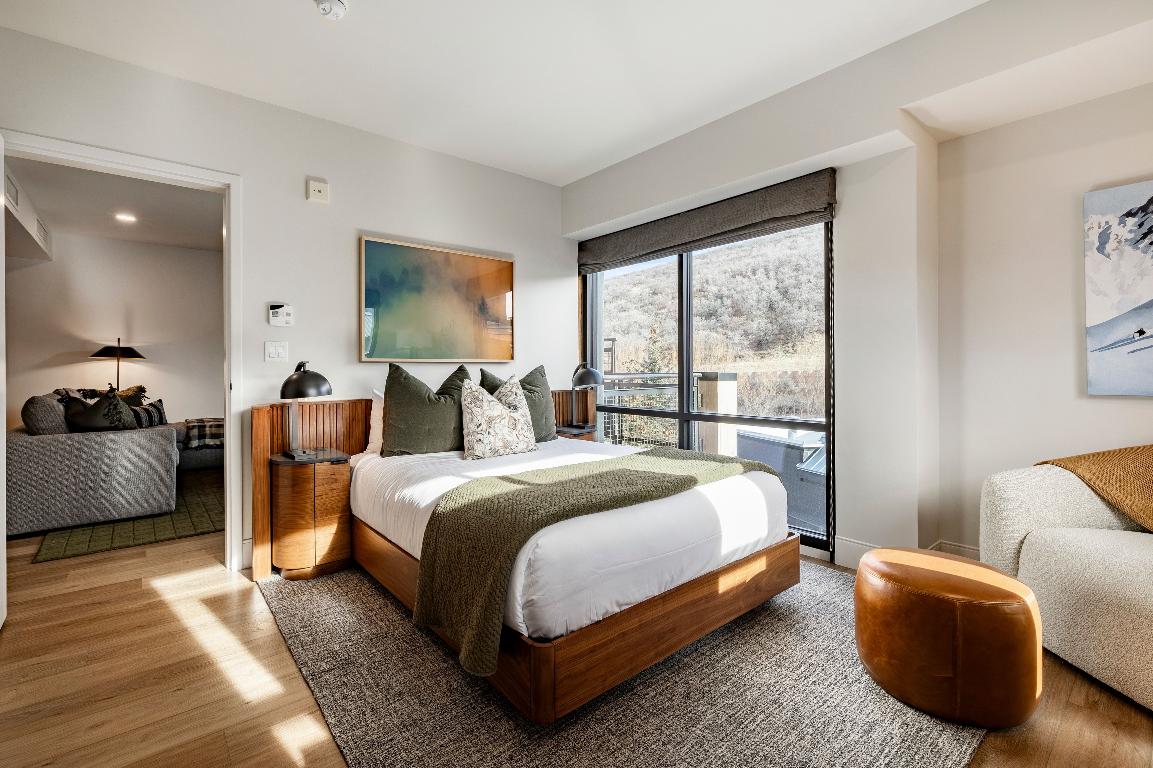 A wide view of a hotel room with a bed, sofa, artwork, and a doorway to another room.