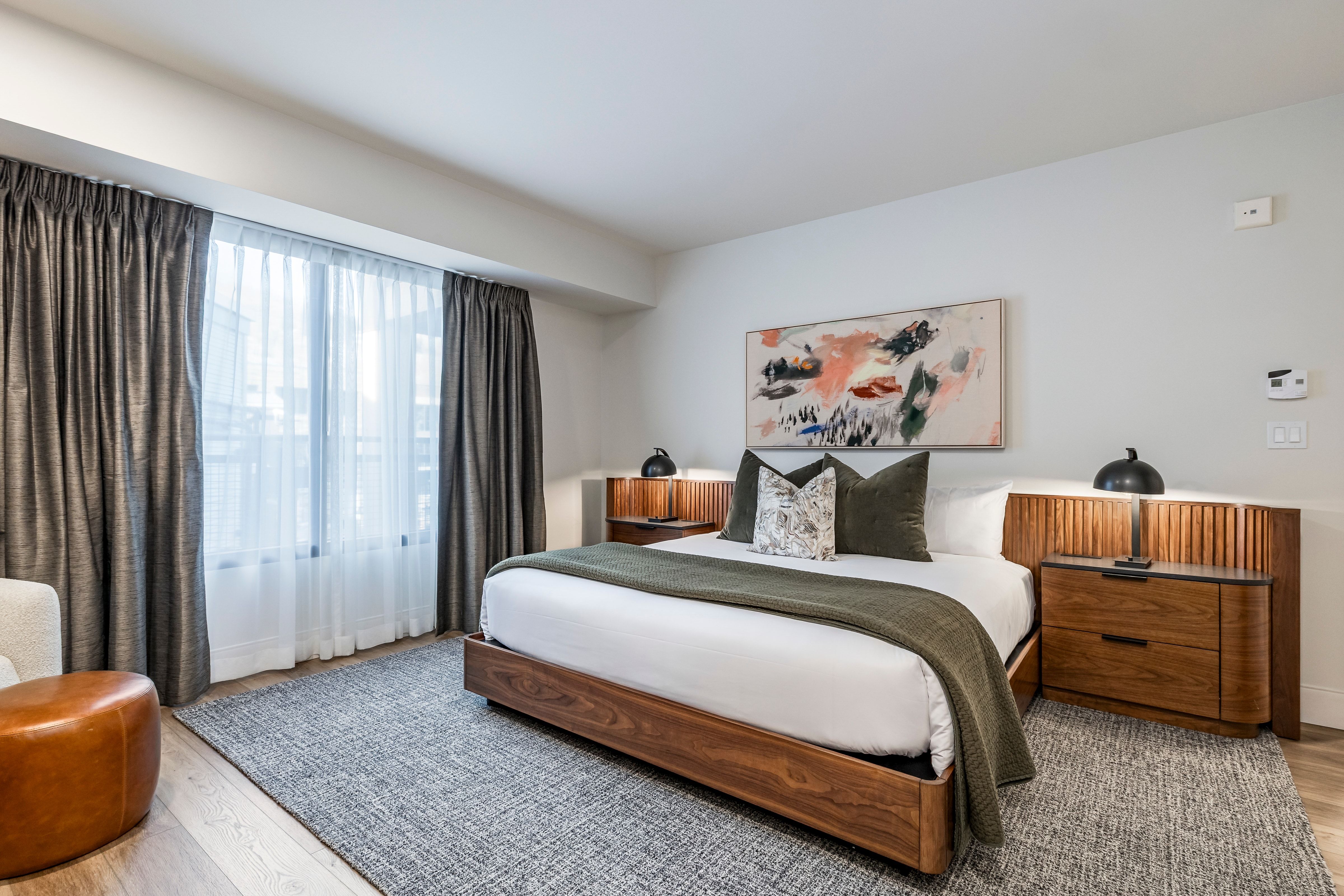 A wide view of a hotel room with a bed, nightstands, and a painting on the wall.