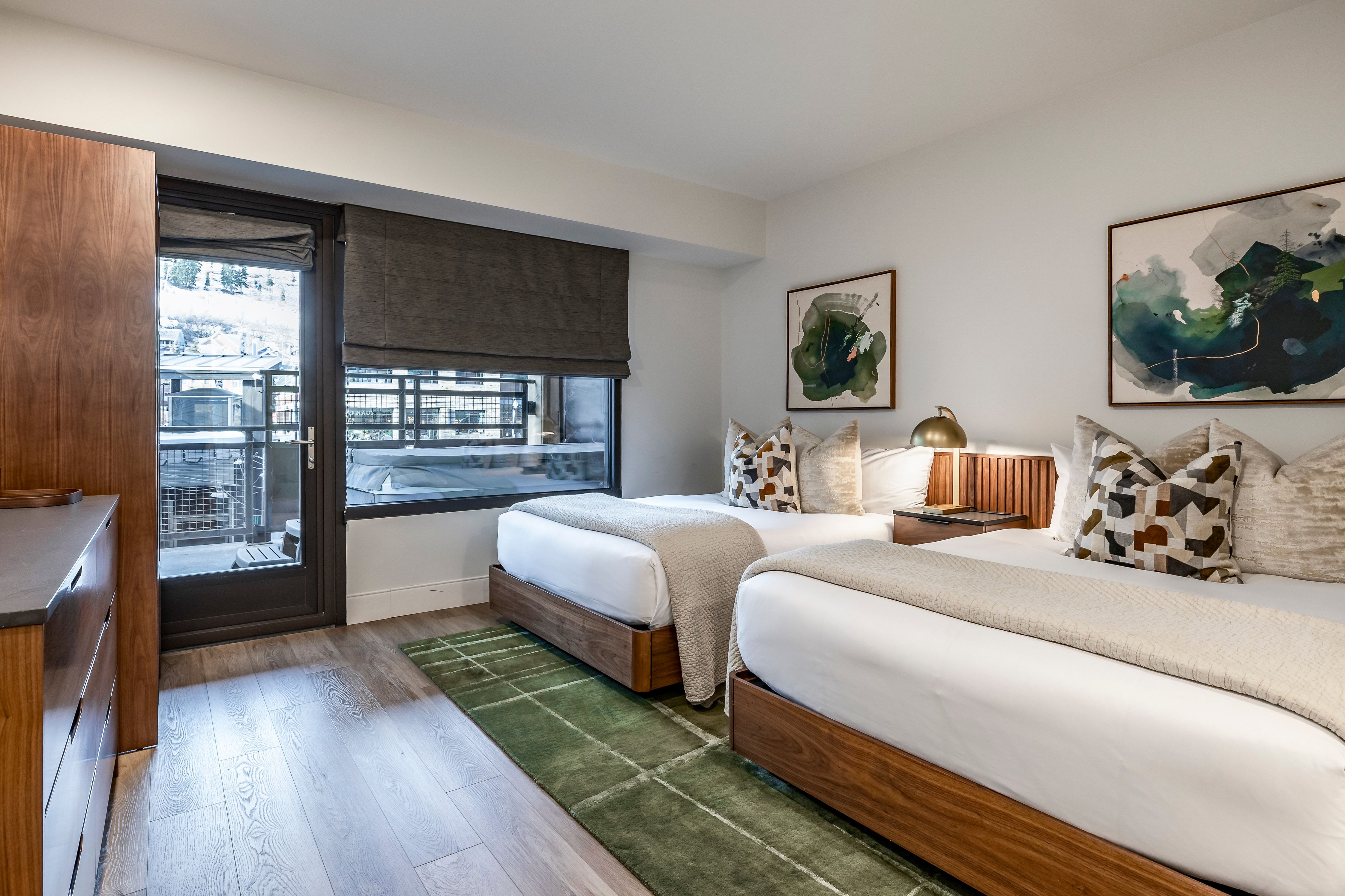 A hotel room with two beds, a green rug, and artwork on the walls.