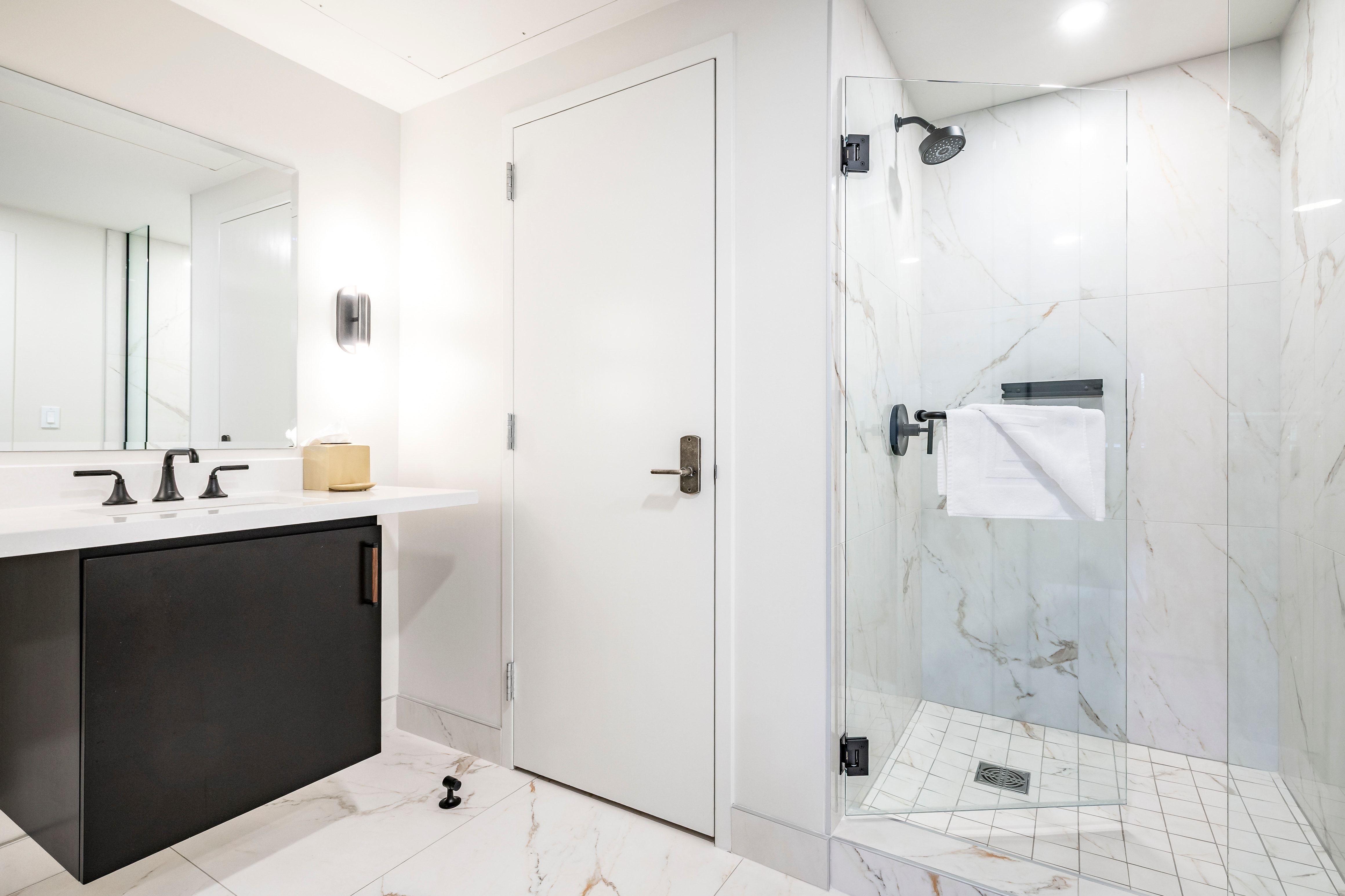 A modern bathroom with a glass-enclosed shower, marble tiles, and black fixtures.