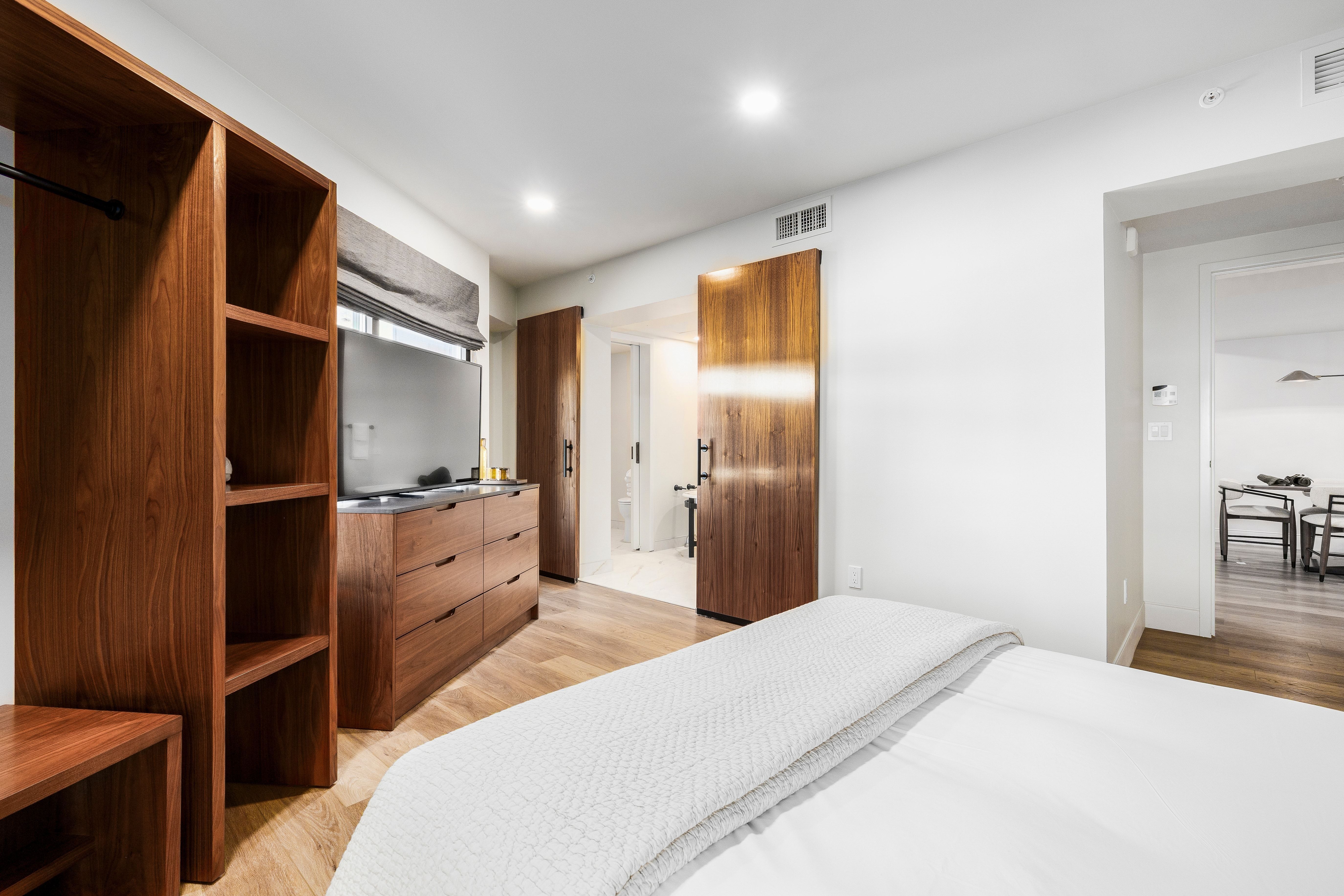 A wide view of a modern hotel room with a bed, dresser, closet, and TV
