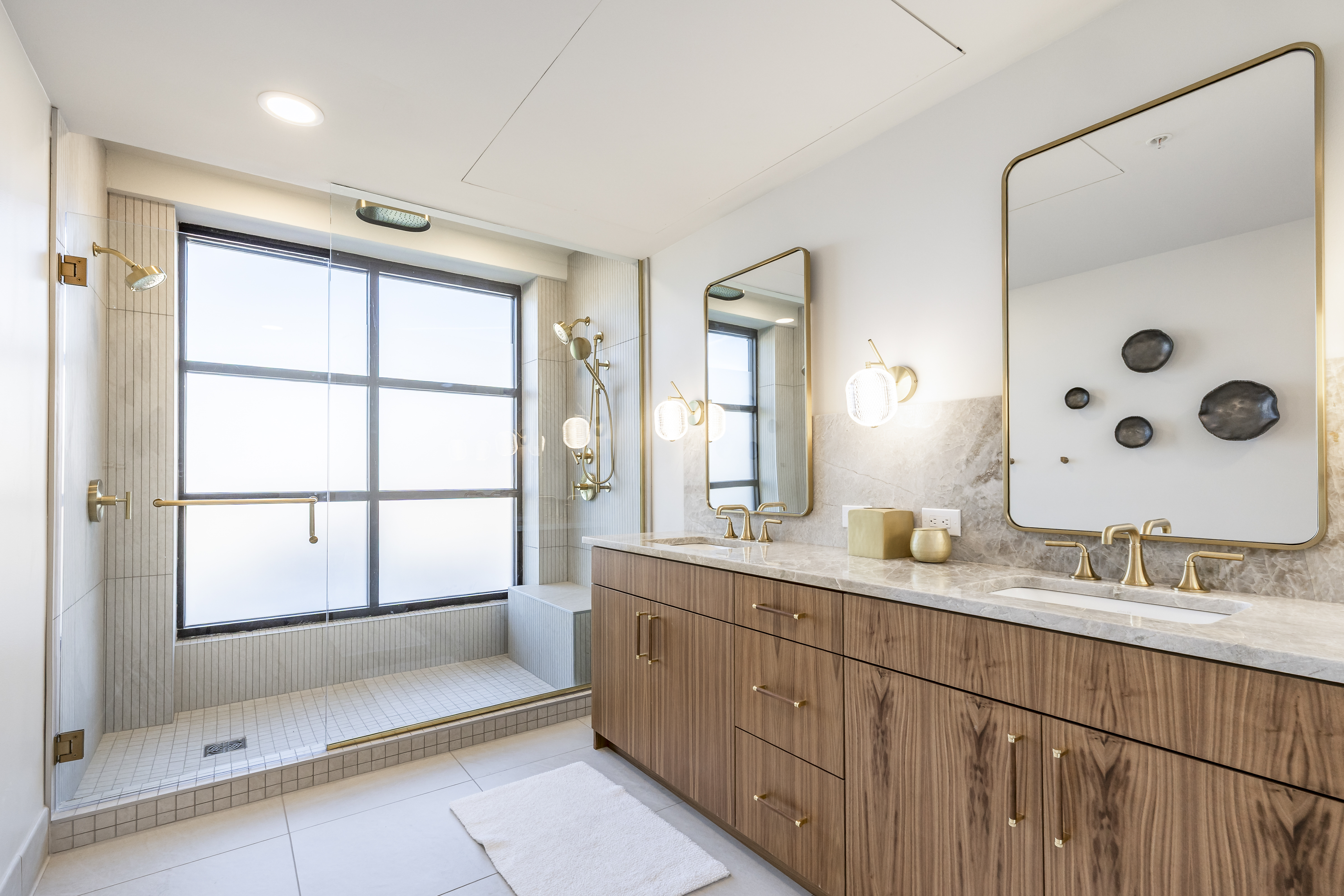 A modern bathroom with a large vanity, a walk-in shower, and a window.