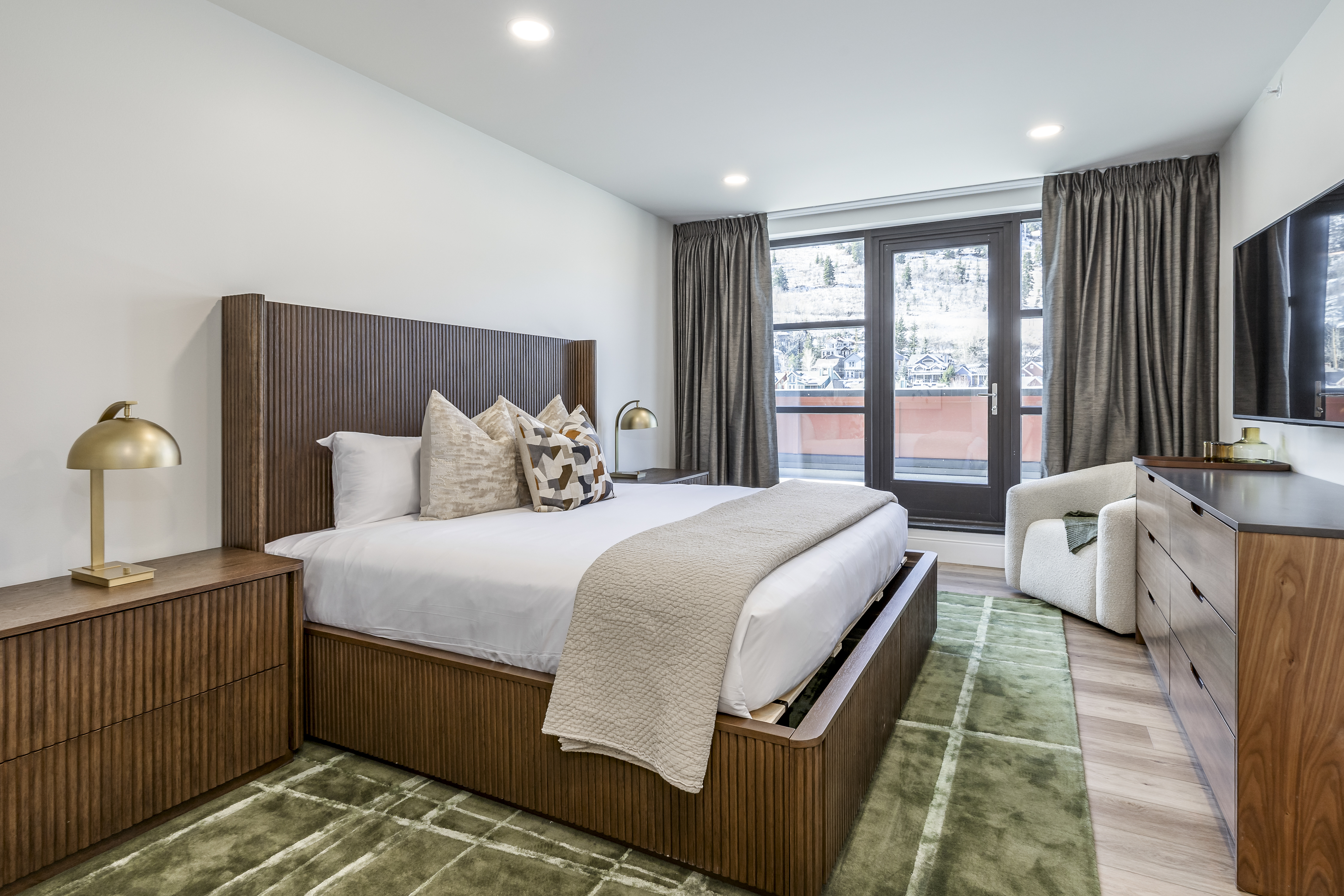 A wide view of a modern hotel room with a large bed, dresser, chair, and TV.