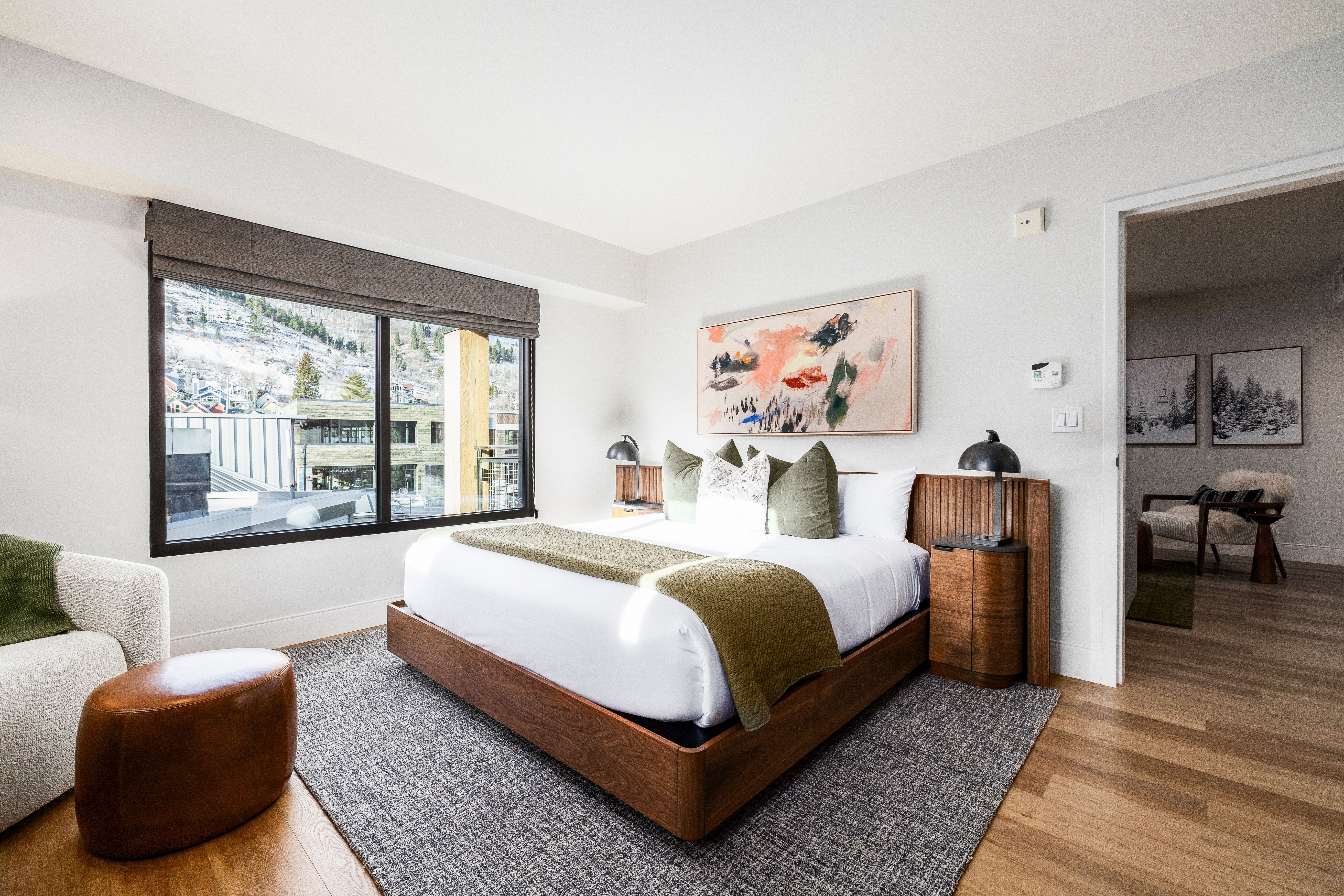 A wide view of a hotel room with a bed, nightstand, and window.