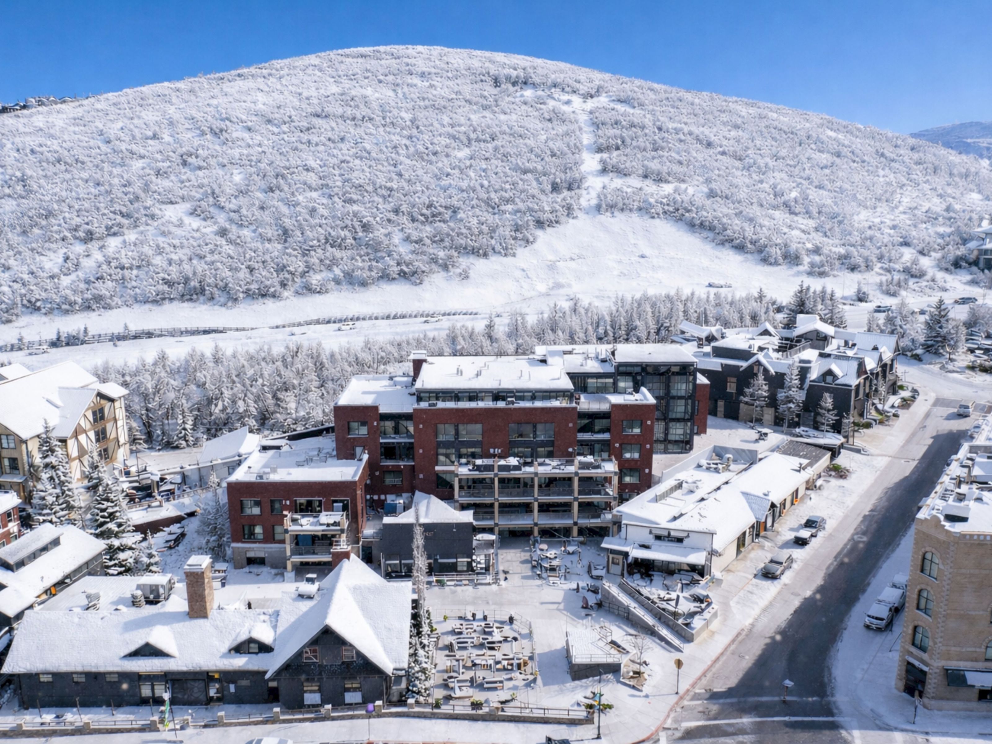 A snowy aerial view of a hotel complex with a mountain in the background.